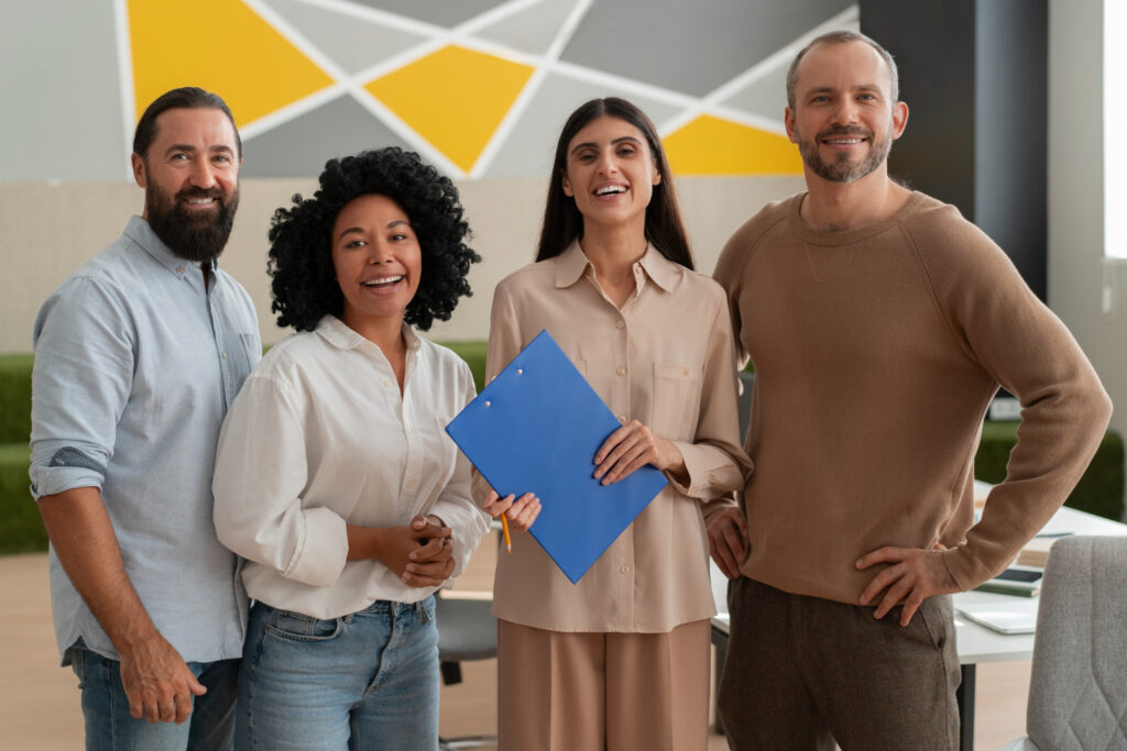 4 pessoas aparecem uma do lado a da outra. Da esquerda para a direita. Homem branco com barba de blusa social azul claro, mulher negra de blusa social branca, mulher branca de blusa sicial bege e homem branco com blusa de linho bege escuro